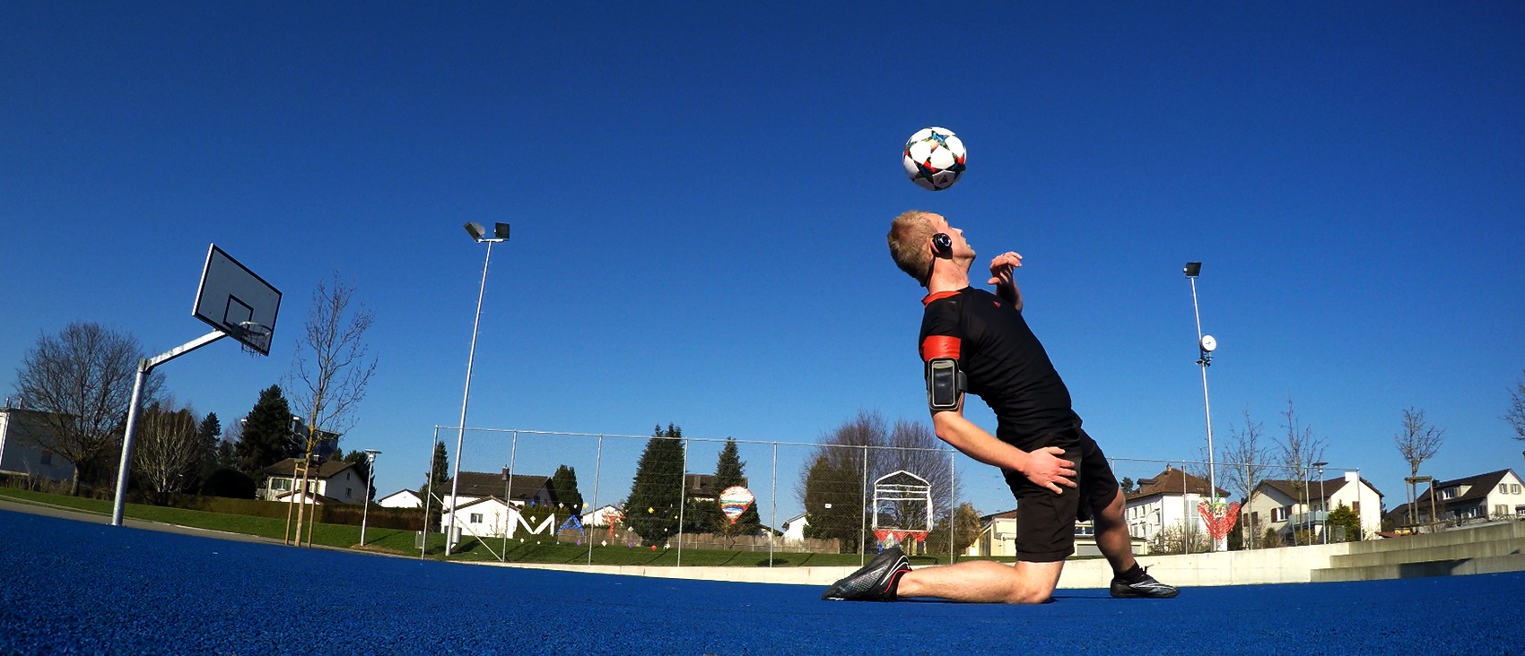 Aeroskiller kontrolliert den Ball in tiefer Balance-Position auf einem blauen Court — Freestyle-Football-Trick in der Ostschweiz.
